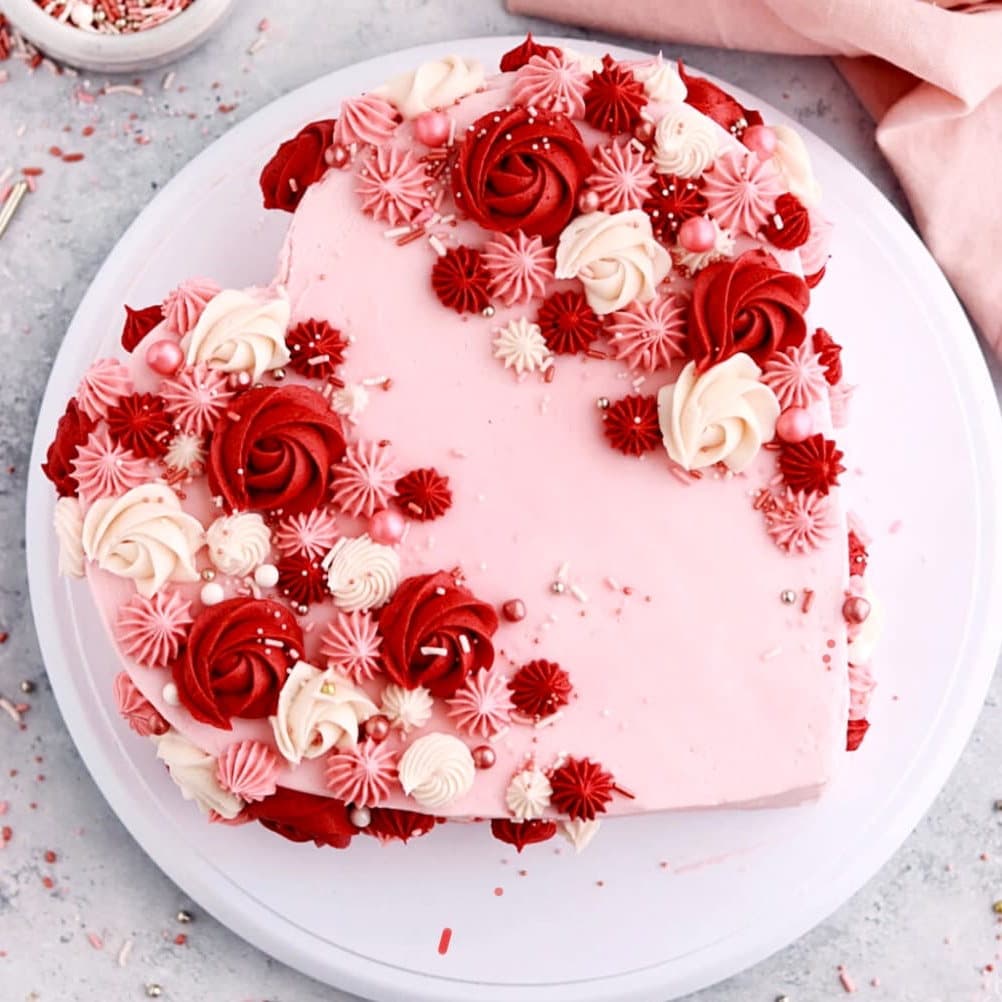 Pink heart shaped cake covered in red and white buttercream rosettes