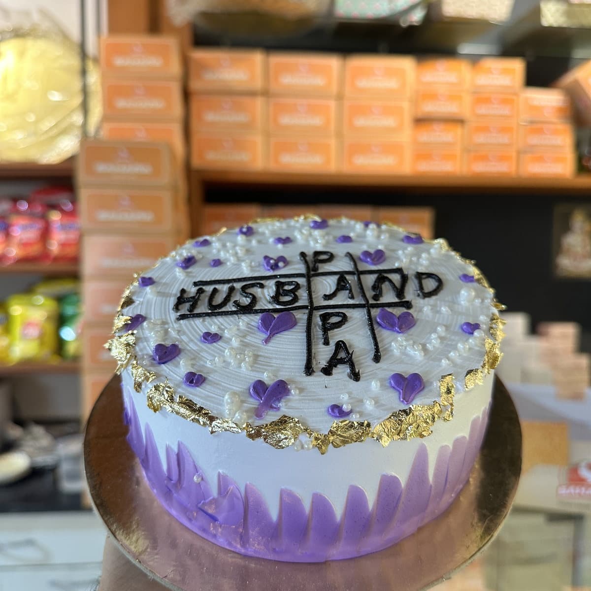 Purple and white anniversary cake spelling Husband and Papa in gold letters